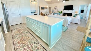 A spacious kitchen with a large island, a dining area with a chandelier, and a living room with a fireplace.