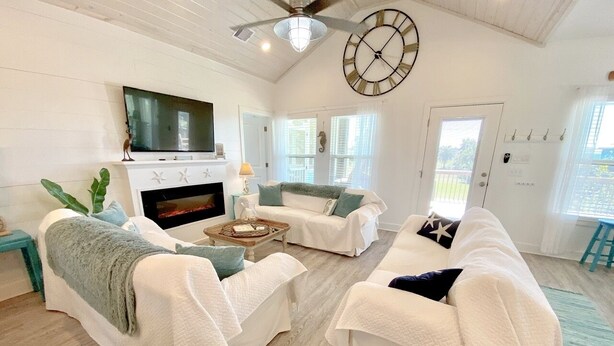A spacious living room with a fireplace, white sofas, a coffee table, and a large wall clock.