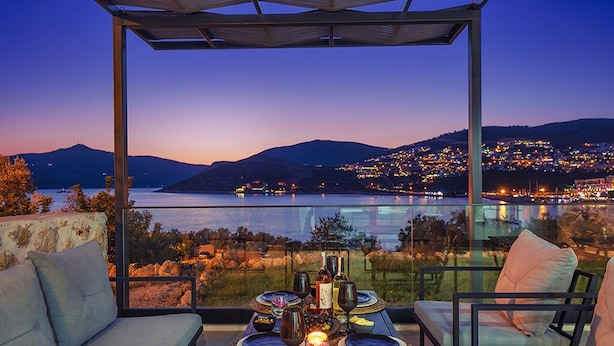A terrace with a table set for dining, overlooking a scenic view of a lake and city lights at dusk. - Villa Nana, A Modern 1 Bedroom Property in Komurluk (Antalya)