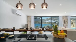 A modern kitchen with a dining area, large windows with a view, and a fruit basket on the table. - Villa Nana, A Modern 1 Bedroom Property in Komurluk (Antalya)