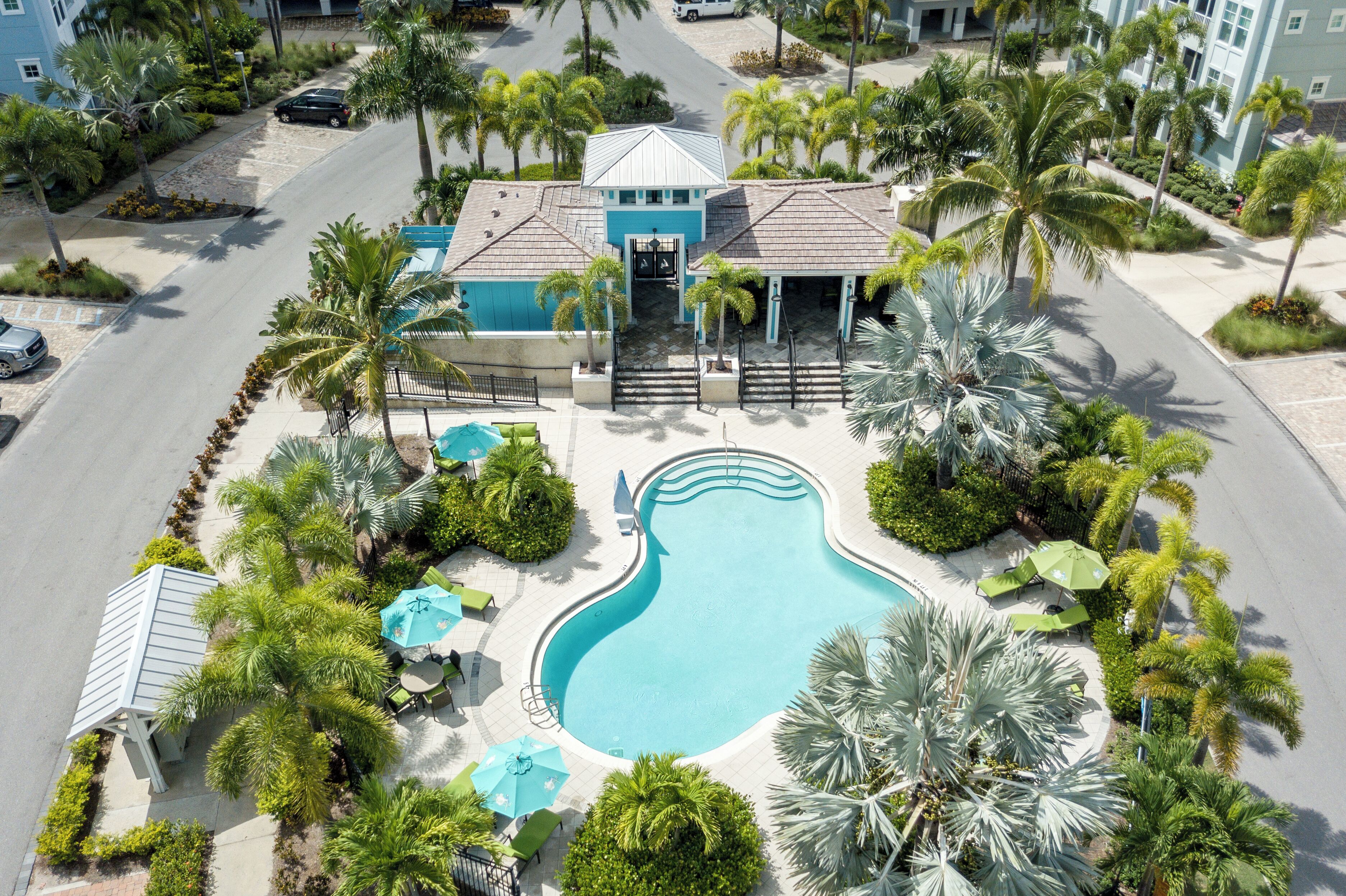 An aerial view of a resort with a swimming pool, palm trees, and a building with a blue roof.