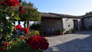 Un patio con suelo de adoquines, un edificio de piedra con techo de tejas y plantas en macetas.