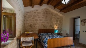Un dormitorio con pared de piedra, vigas de madera en el techo, cama, mesita de noche y una silla.