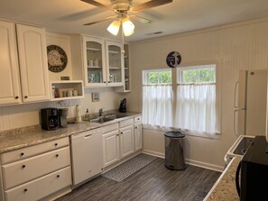 A kitchen with white cabinets, a granite countertop, a coffee maker, a sink, and a window with curtains. - Relax at this beautiful Historic Intracoastal Waterlily Cottage + Game Room (Coinjock)