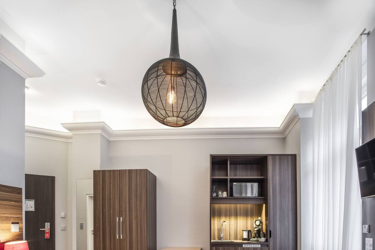 Habitación de hotel moderna con una cama grande, un escritorio, una kitchenette y un televisor.