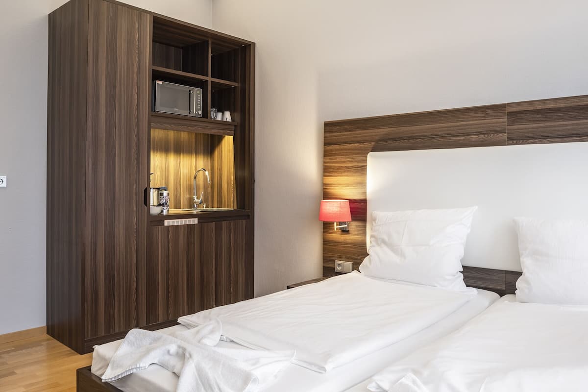 Una habitación de hotel moderna con una cama grande, cabecera de madera, armario empotrado, mesita de noche y una lámpara.