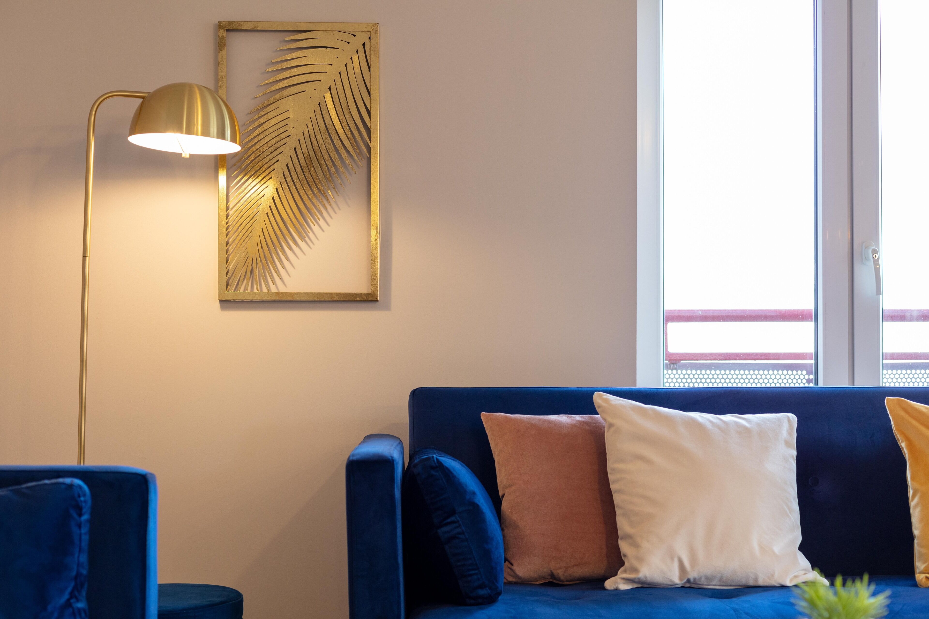 A modern living room with a blue sofa, a gold floor lamp, and a framed leaf artwork on the wall.