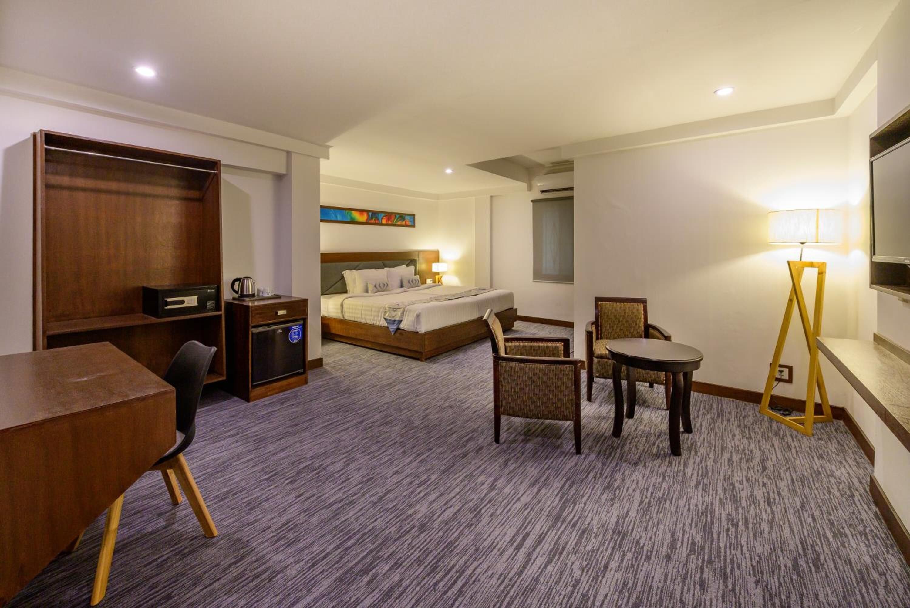 Une chambre d’hôtel comprenant un lit, un bureau, une chaise, une petite table et une lampe.