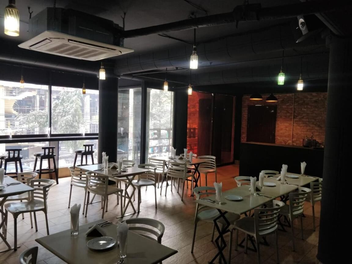 A restaurant with tables and chairs, large windows, and hanging lights.