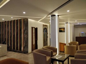 Een moderne hotellobby met een receptiebalie, een zithoek en een grote pilaar.
