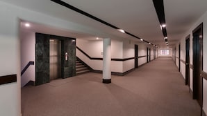 A long, narrow hallway with a marble elevator, a staircase, and a carpeted floor. - Hotel Zakaria International (Dhaka)