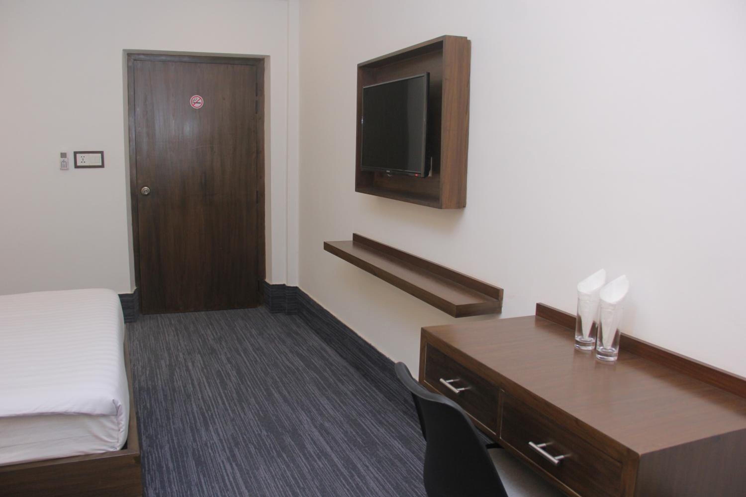 A hotel room with a bed, a desk with drawers, a mounted TV, and a door with a no-smoking sign.