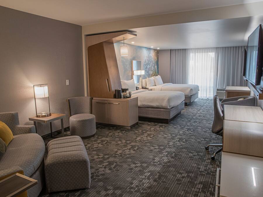 Une chambre d’hôtel avec un canapé, deux lits, un bureau, une télévision et une lampe.