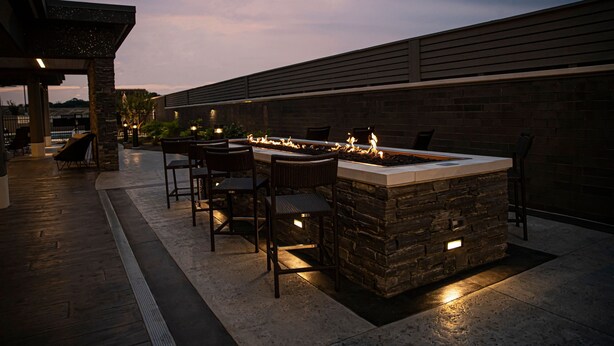 An outdoor patio with a stone fire feature, seating, and a view of the city skyline. - Courtyard by Marriott Greenville Mauldin (Greenville)
