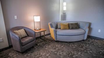 A room with a grey armchair, a sofa with patterned cushions, a floor lamp, and a standing lamp.