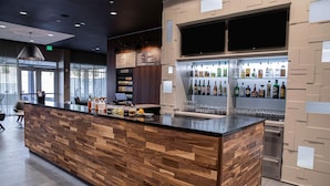 A modern bar area with a wooden counter, a digital menu board, and a variety of liquor bottles. - Courtyard by Marriott Greenville Mauldin (Greenville)