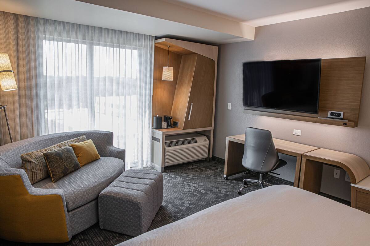 A hotel room with a sofa, a desk, a chair, a TV, and a bed.