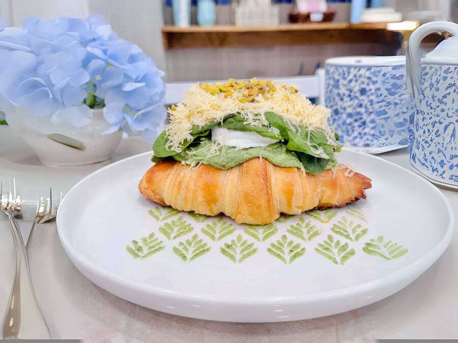 A croissant with spinach and cheese on a white plate, accompanied by a blue and white patterned cup and a vase of blue flowers.