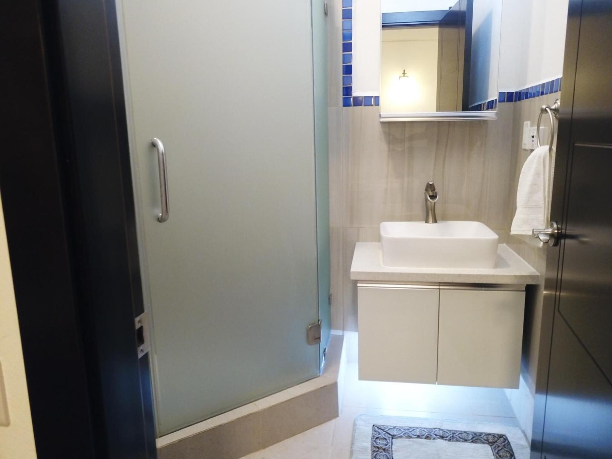 Un baño con un lavabo blanco, un espejo encima y una toalla colgada en un perchero.