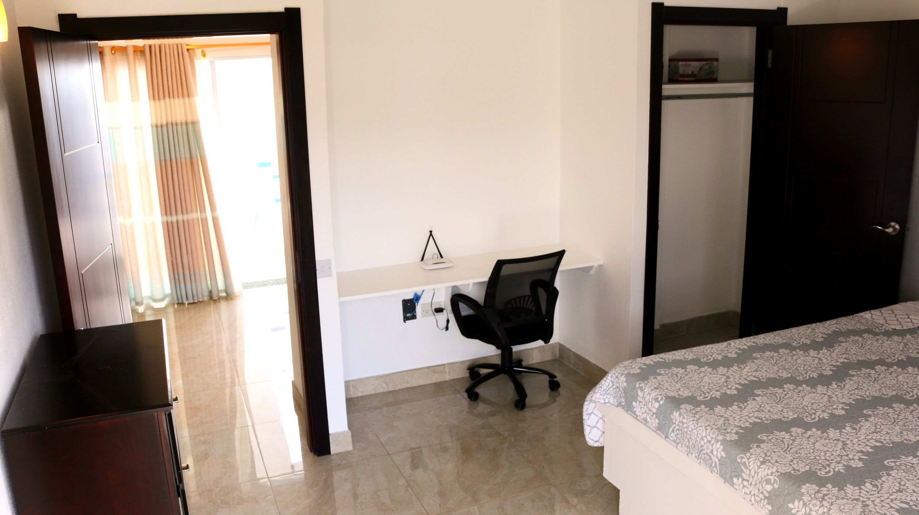 A bedroom with a bed, a desk with a chair, a wardrobe, and a door leading to another room.