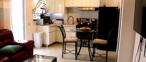 A compact kitchen with a dining area, a glass coffee table, and a leather sofa.