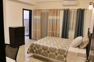 Habitación con cama, cómoda y silla. Se ve un baño a través de una puerta abierta.