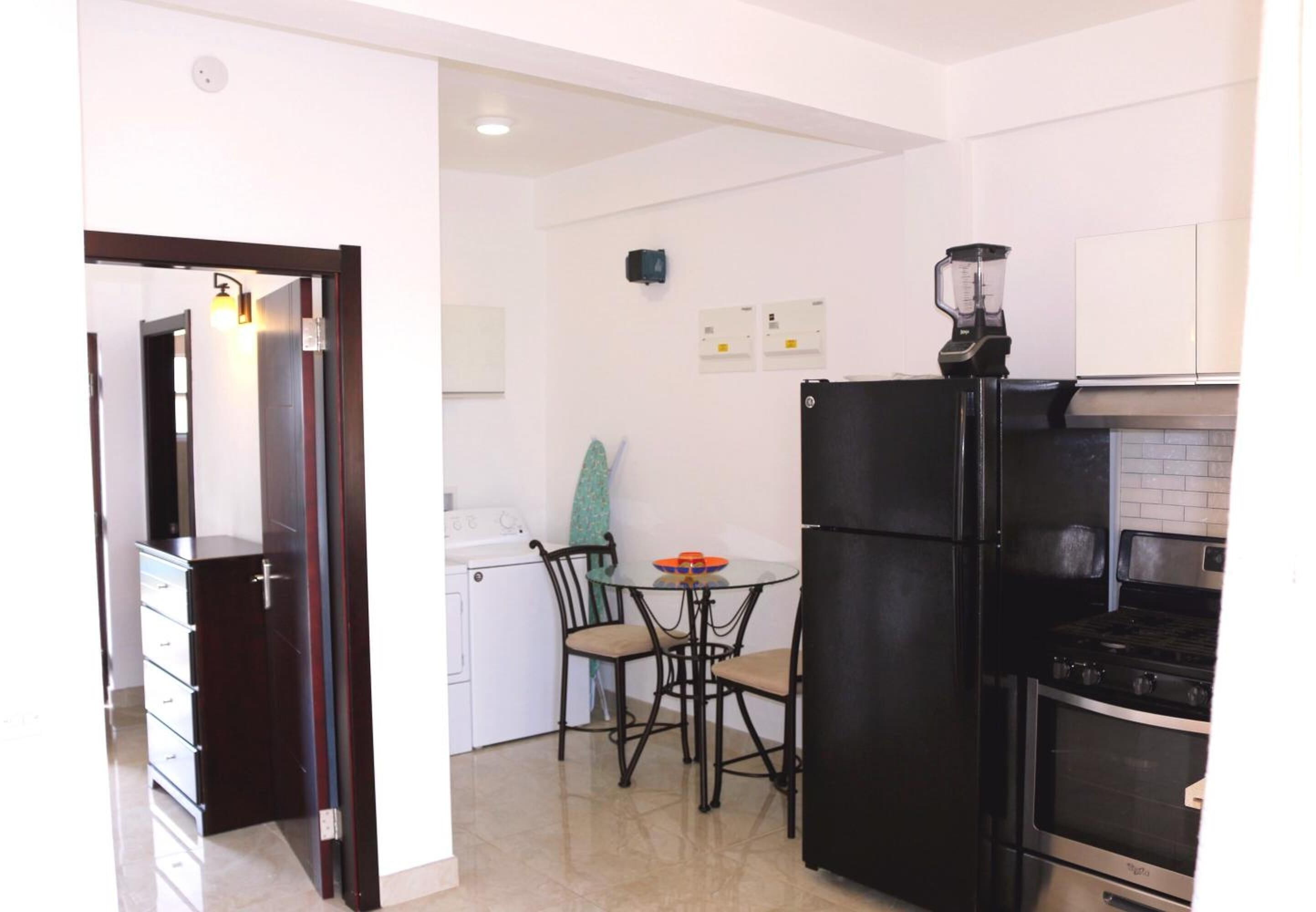 A compact kitchen with a black refrigerator, a stove, and a small dining table with chairs.