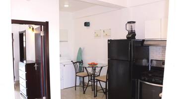 A compact kitchen with a black refrigerator, a stove, and a small dining table with chairs.