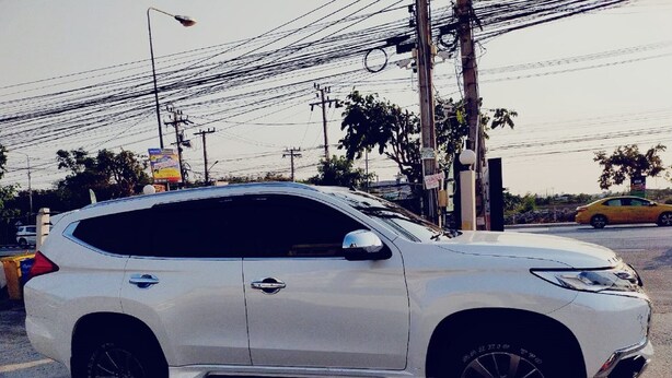 A white SUV parked on a street with overhead power lines and a yellow car in the background.