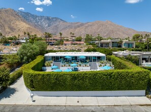 A modern house with a pool, surrounded by a well-maintained hedge, and mountains in the background.