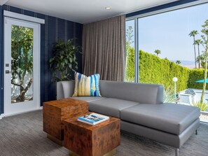 Un soggiorno moderno con un divano grigio, un tavolino in legno e un'ampia finestra vista piscina e verde.