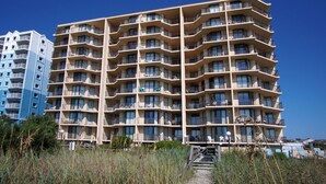 A multi-story hotel with balconies, a pathway leading to the entrance, and a clear blue sky.