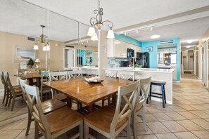 A spacious dining area with a wooden table and chairs, a kitchen with white cabinets and a blue accent wall, and a tiled floor. - Wow! Gorgeous end condo w/panoramic ocean views, 2 master suites, large pool, spacious balcony (North Myrtle Beach)
