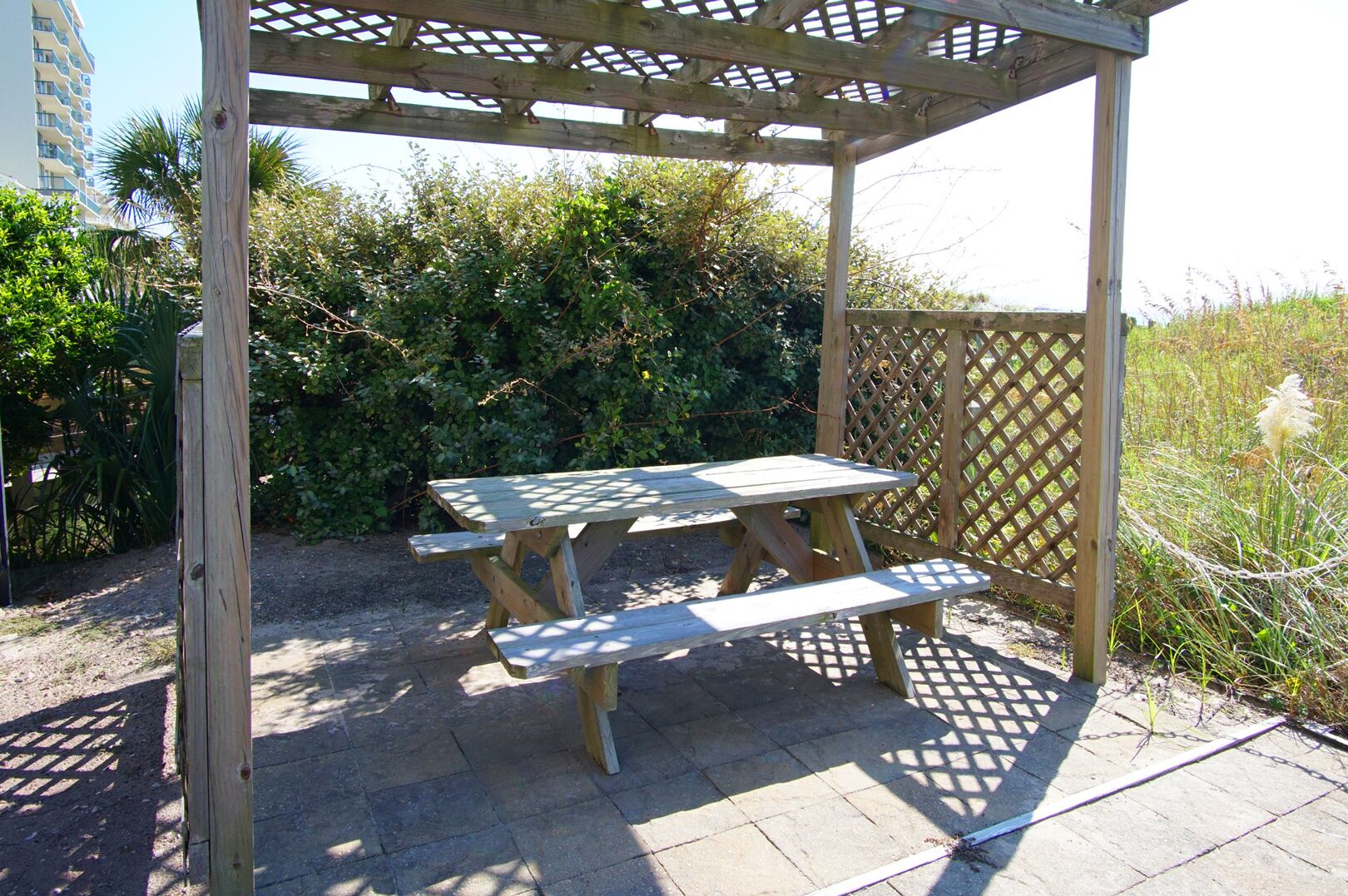 Een houten pergola met een picknicktafel en banken in een tuin.