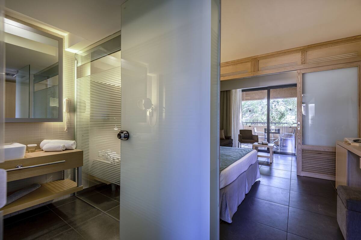 Een moderne hotelkamer met een badkamer, inclusief een douchecabine van glas, een wastafel met spiegel en een bed met uitzicht op het buiten.