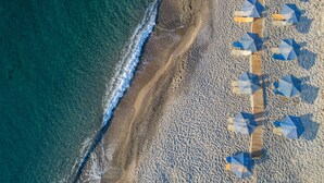 Vista aérea de una playa con un camino de madera y sombrillas a rayas.