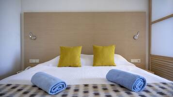 Una cama bien hecha con una colcha estampada, dos almohadas amarillas brillantes y dos toallas azules enrolladas.