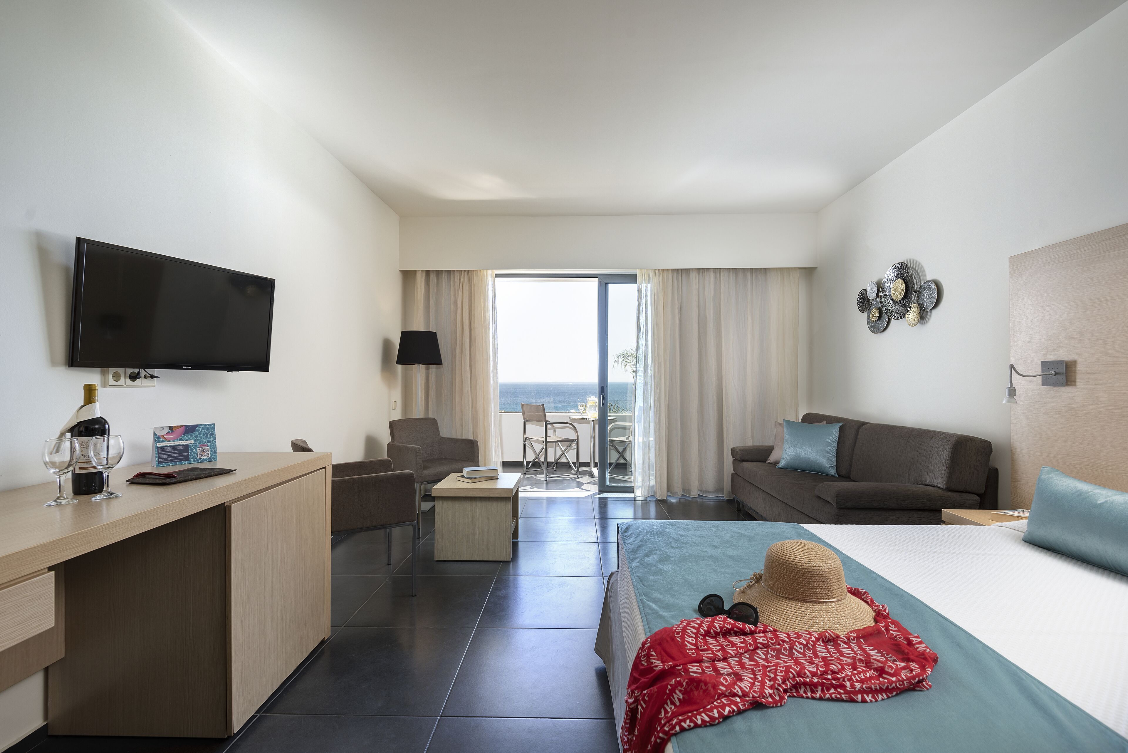 A modern hotel room with a bed, a desk, a TV, a balcony with a view, and a dining area.