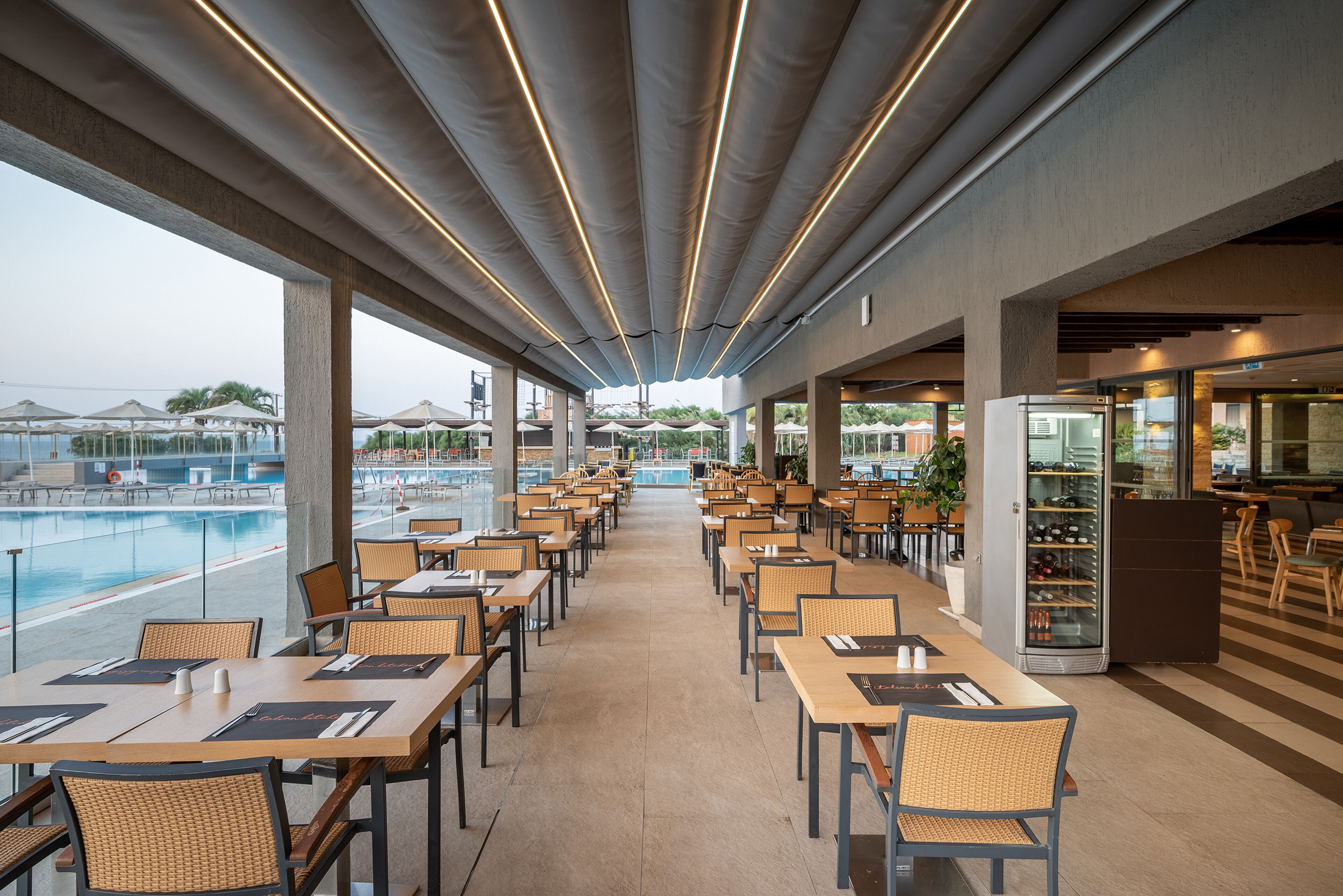 A spacious outdoor dining area with tables and chairs, overlooking a pool and poolside umbrellas.