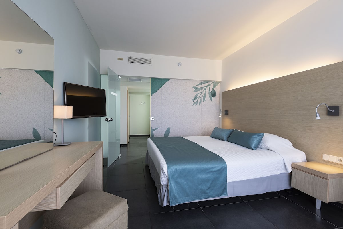 Een moderne hotelkamer met een bed, nachtkastje, televisie en bureau met stoel.