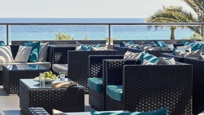 Un balcón con mobiliario de mimbre, una mesa con vasos y un plato de fruta, y vista al mar.