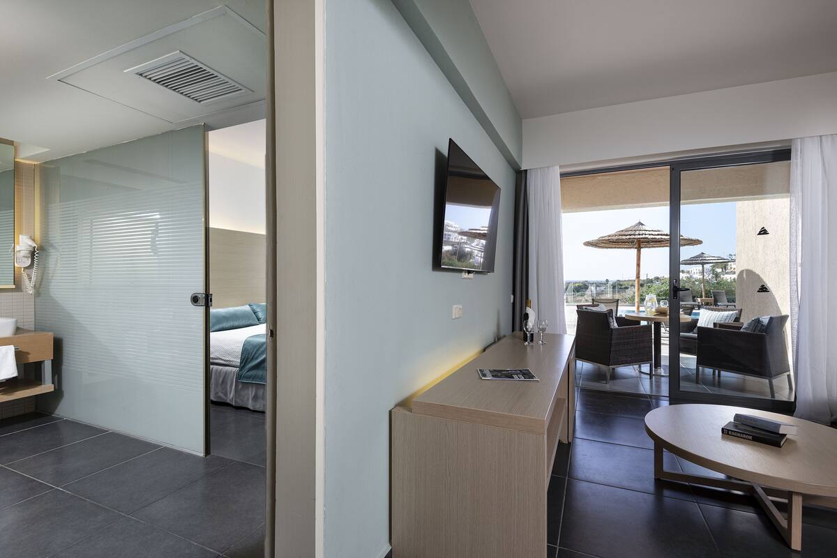 Een moderne hotelkamer met een grote schuifpui die uitkomt op een buitenzitgedeelte met parasols.