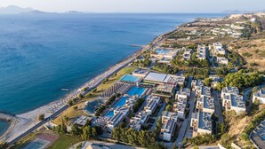 Vista aérea de un resort costero con varias edificaciones, una piscina y una zona de playa.