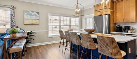 A modern kitchen with a central island, bar stools, and a hanging light fixture.