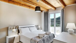 Ein modernes Schlafzimmer mit Holzboden, einem großen Bett mit gemustertem Überwurf, Nachttischlampen und Blick auf eine Landschaft durch das Fenster.