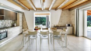 Eine moderne Küche mit weißen Schränken, ein Essbereich mit Tisch und Stühlen und Blick ins Grüne.
