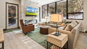 A modern living room with a stone fireplace, a large window with a snowy view, a flat-screen TV, and a cozy seating area.