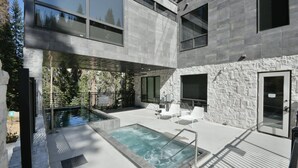 A modern outdoor pool area with a stone wall, a hot tub, and lounge chairs.