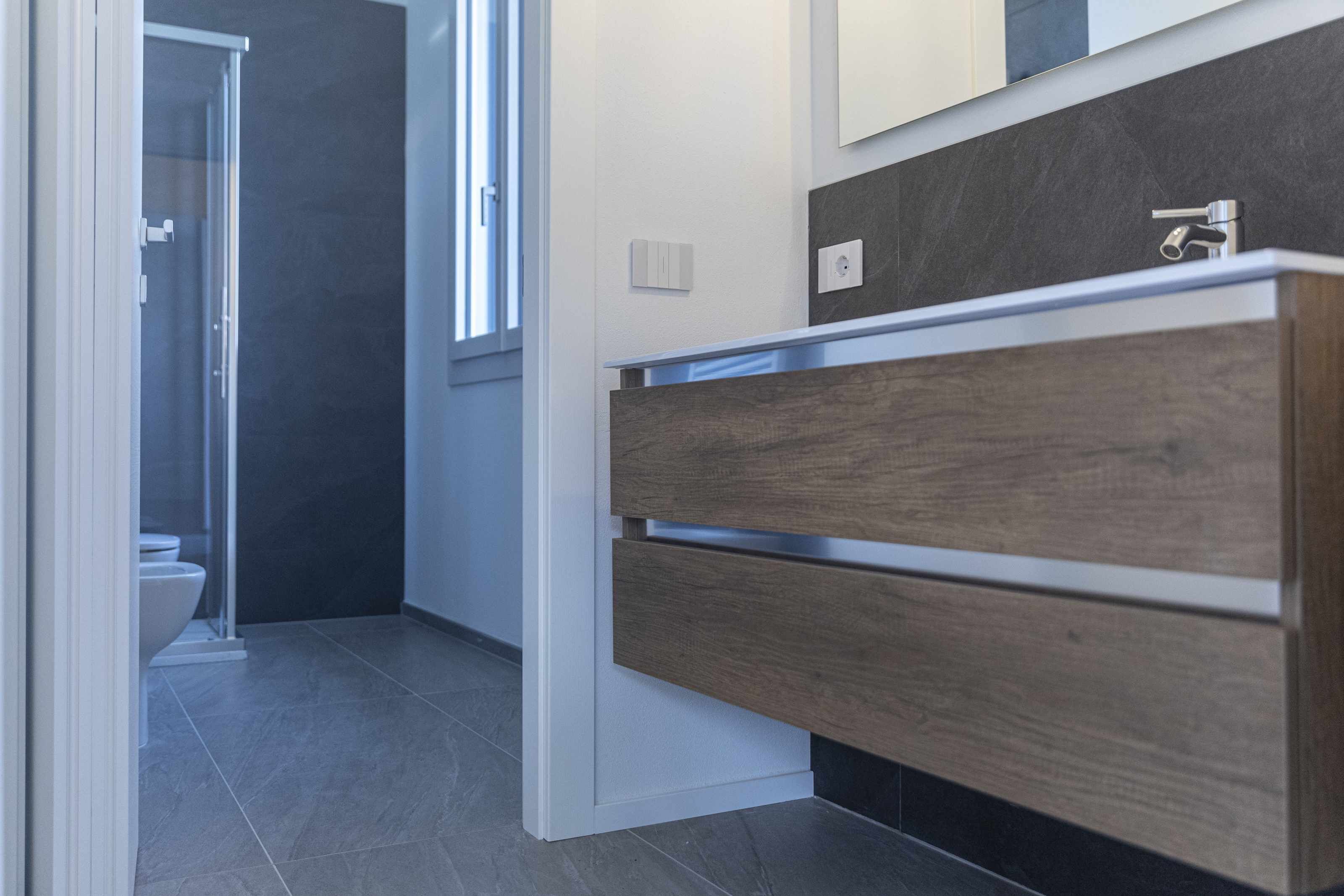 A modern bathroom with a wooden vanity, a glass shower enclosure, and a toilet.