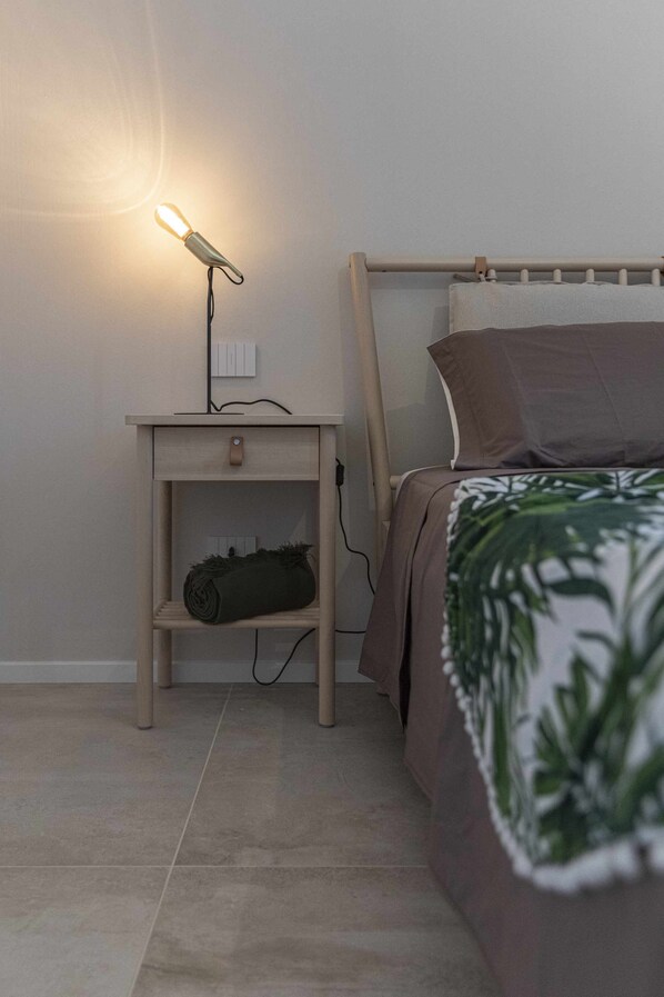 A bedroom with a wooden bed frame, a nightstand with a lamp, and a shelf with a rolled-up blanket. - CA ’DEL RE’ SCARTOZZ Riva dei Bruti (Gavirate)